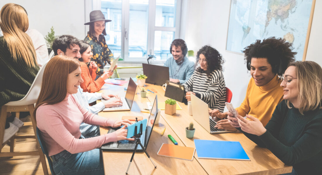 Young co-workers team talking during startup - Happy people planning a new project in creative coworking office - Technology, entrepreneur, marketing concept - Focus on left girl face with red hair